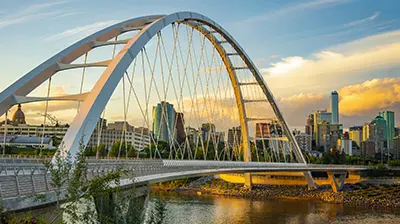 View of an arched bridge going over a river with a city in the background 